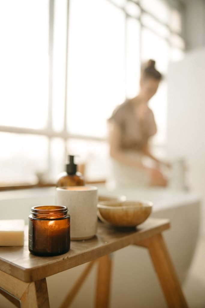 lighted-candle-on-the-wooden-table-6811180 Warm, calming bathroom scene with candle and beauty products. Perfect for relaxation themes.